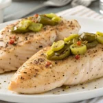 Two seasoned Mississippi Chicken on a white plate, topped with sliced pepperoncini peppers and lightly sprinkled with black pepper.