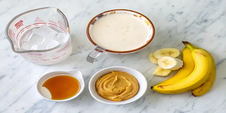 Ingredients for peanut butter banana smoothie including bananas, peanut butter powder, milk, and granola.