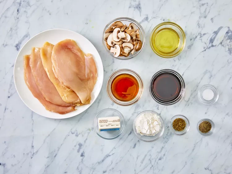 Flat lay of Chicken Marsala ingredients including chicken, mushrooms, Marsala wine, and seasonings